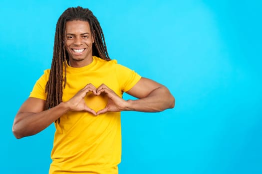 Latin man with dreadlocks representing a heart in the shape with hands in studio with blue background