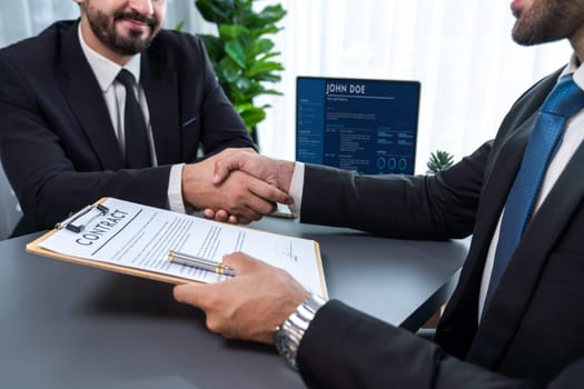 Two professionals successfully close business deal with closeup handshake, sealing the partnership agreement. Legal document and handshaking as formal agreement between two companies. Fervent