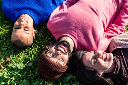 three young friends enjoying a sunny day lying in the grass, concept of friendship and relax in the park