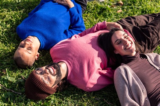 three young friends resting in a sunny day lying in the lawn, concept of friendship and relax in the park