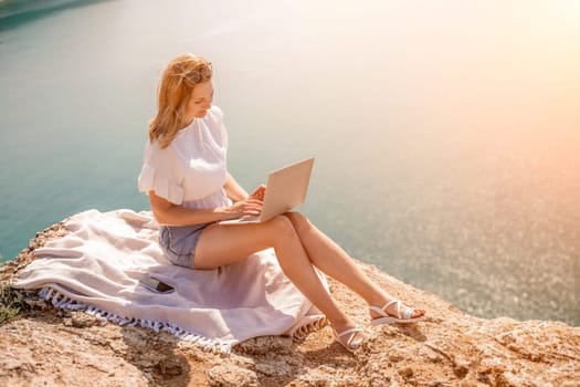 Freelance woman working on a laptop by the sea, typing away on the keyboard while enjoying the beautiful view, highlighting the idea of remote work