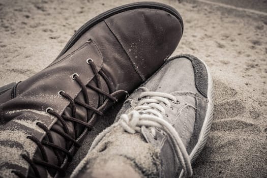 Shoes of man and woman lying next to each other on the sand.
Sepia colors.