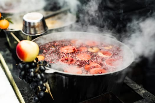Person buy hot fruit and berries mulled winebeverage at street food market. Fresh drinks in pots at fair outdoors