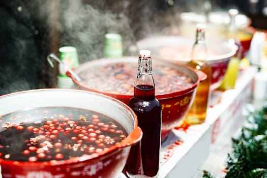 Beverages berries hot mulled wine in pots in street food market at Christmas time. Colorful festive hot drinks at fair xmas festival outdoors closeup