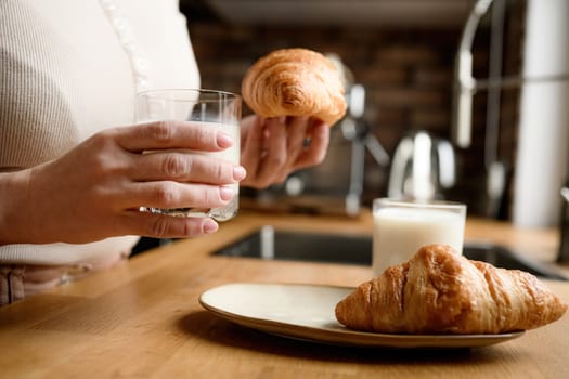 Girl has a breakfast with milk and croissants at kitchen