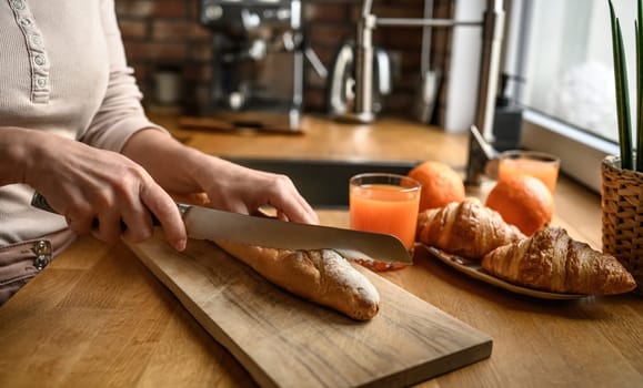 Girl hand cut french baguette with knife at kitchen. Tasty rustic fresh bread from France for breakfast meal