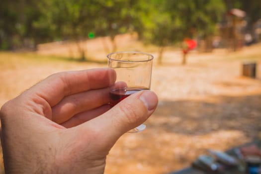 Man hand holding a shot glass with red wine at a social meeting outdoor.