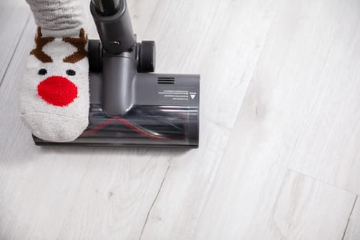 An overhead view of one foot trampling the end of a vacuum cleaner. Keeping things tidy by cleaning the floorboards frequently.