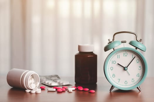An alarm clock with a pile of pills and medicine bottles on a wooden table for time management and healthcare concept.