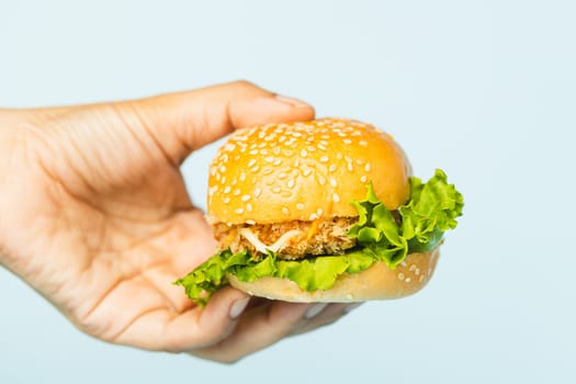 Hand holding a delicious hamburger on blue background for bakery, food and eating concept