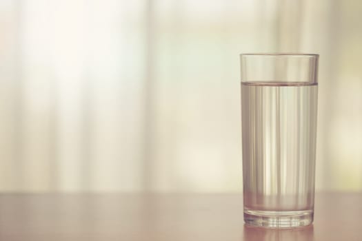 Glass of drinking water on blurred white curtain background with sun light effect for healthy drinking and beverages concept