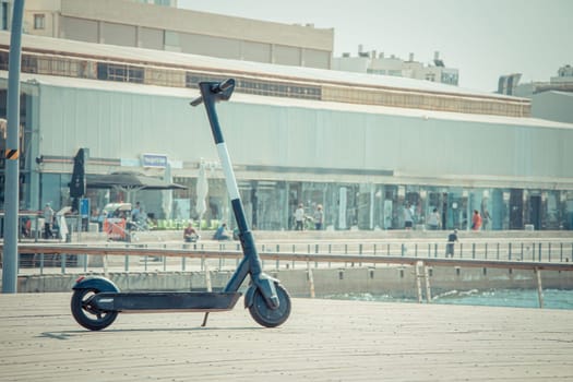 Black electric scooter parking on a deck at Tel Aviv Port commercial district on a summer sunny day. Close up selective focus with copy space.