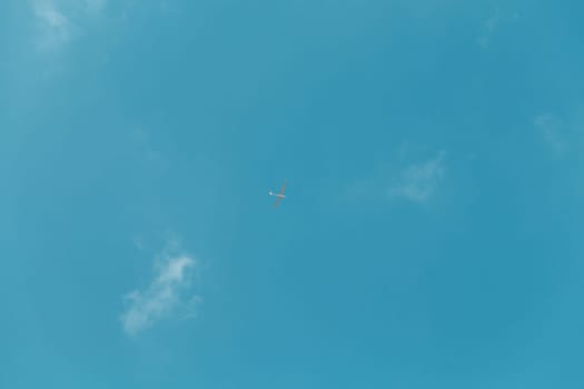 Glider gliding in blue sky from below.