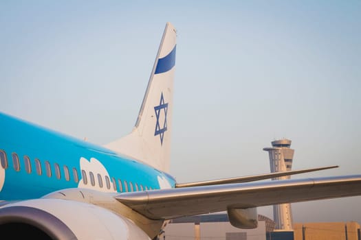 Tailplane of an airplane with a drawing of the Israeli flag and the air traffic control tower of Ben Gurion Airport on sunrise.