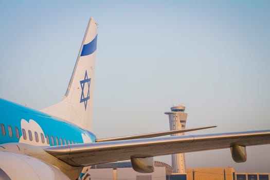 Tailplane of an airplane with a drawing of the Israeli flag and the air traffic control tower of Ben Gurion Airport on sunrise.
