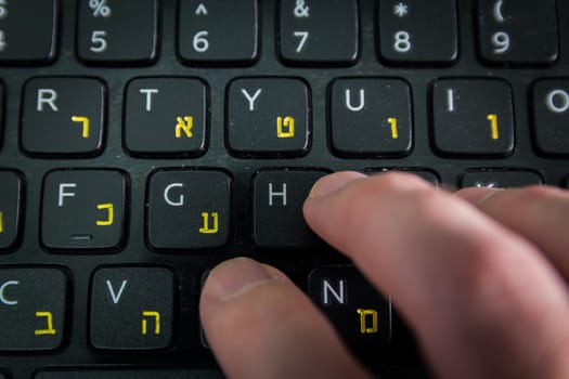 Man typing on a keyboard with letters in Hebrew and English - Laptop keyboard - Top View - Close up_Dark atmosphere