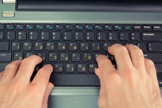 Man typing on a keyboard with letters in Hebrew and English - Laptop keyboard - Top View
