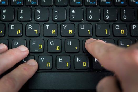 Man typing on a keyboard with letters in Hebrew and English - Laptop keyboard - Top View - Close up_Dark atmosphere