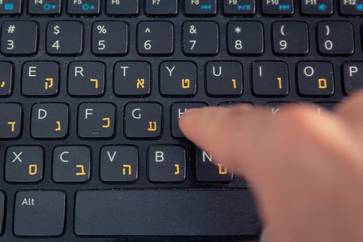 Man typing on a keyboard with letters in Hebrew and English - Laptop keyboard - Top View - Close up