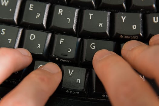 Man typing on a keyboard with letters in Hebrew and English - Wireless keyboard - Top View