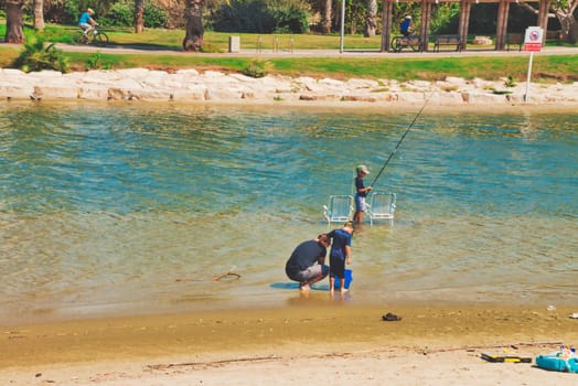 Tel Aviv, Israel - Oct 1, 2019: Father with his children fishing with fishing rod together in the Yarkon River at Tel Aviv city on a sunny summer day.