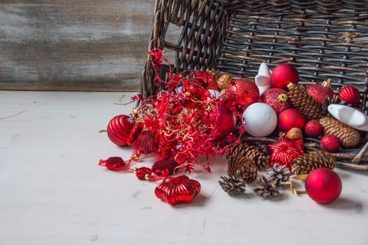 Christmas basket with champagne bottle and glasses, gifts with red satin ribbon, candy canes, pine cones, golden garlands on white wooden background