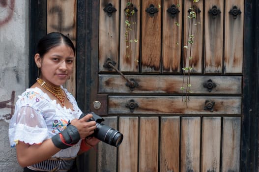 bonita mujer indigena con una camara de fotos profesional dslr junto a una puerta de la calle mirando a camara. High quality photo