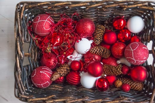 Christmas basket with champagne bottle and glasses, gifts with red satin ribbon, candy canes, pine cones, golden garlands on white wooden background