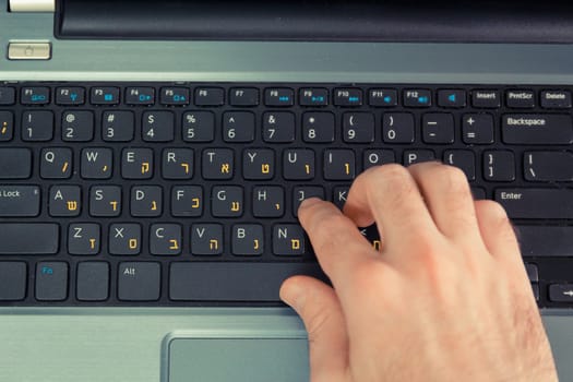 Man typing on a keyboard with letters in Hebrew and English - Laptop keyboard - Top View