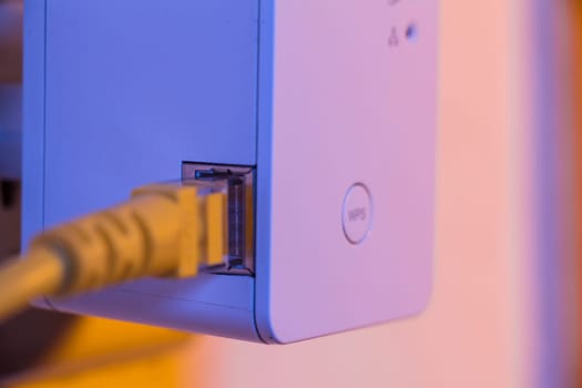 WiFi extender in electrical socket on the wall with ethernet cable plugged in. The device is in access point mode that help to extend wireless network in home or office.