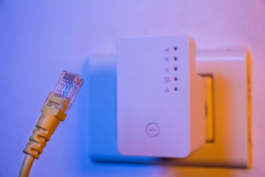 Closeup of ethernet cable. WiFi extender device in electrical socket on the wall on the background. The device is in access point mode that help to extend wireless network in home or office.