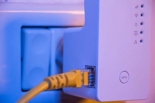 WiFi extender in electrical socket on the wall with ethernet cable plugged in. The device is in access point mode that help to extend wireless network in home or office.