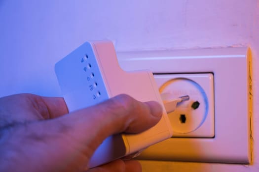 Man insert WiFi repeater into electrical socket on the wall. The device help to extend wireless network in home or office.