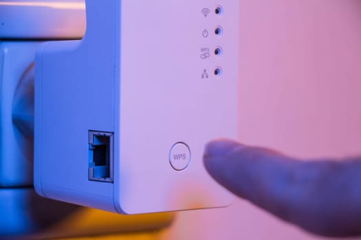 Man press with his finger on WPS button on WiFi repeater which is in electrical socket on the wall. The device help to extend wireless network in home or office.