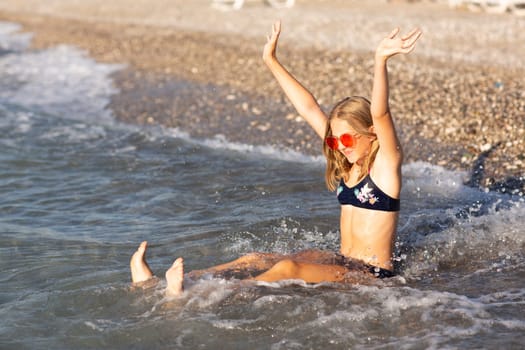 Teenage girl in pink sunglasses having fun on the beach in the sea, playing with waves and splashes. Fun on summer hloiday concept.