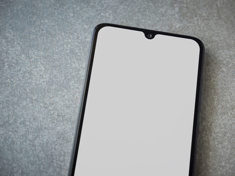 Black mobile smartphone mockup lies on the surface with a blank screen isolated on a porcelain granite ceramic stone background. Top view closeup with selective focus and copy space, cut in the middle