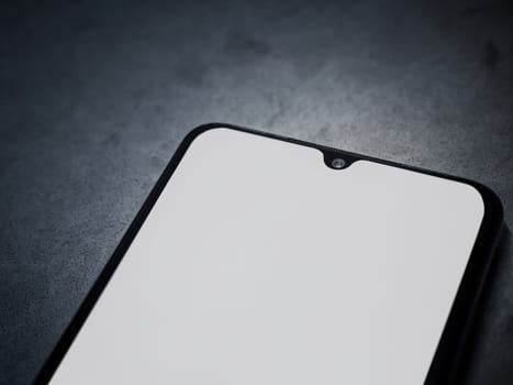 Black mobile smartphone mockup lies on the surface with a blank screen isolated on a dark marble stone background. Top view close up with selective focus and copy space, cut in the middle.