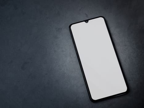 Black mobile smartphone mockup lies on the surface with blank screen isolated on dark marble stone background. Top view flat lay with copy space.