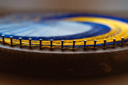 Colored thread mandala on a wooden board with nails. Mandala Moon Harmony Sun esotericism and psychology pictures from yellow and blue silk threads