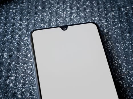 Black mobile smartphone mockup lies on the surface with blank screen isolated on a metallic background. Top view close up with selective focus and copy space, cut in the middle.