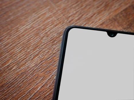 Black mobile smartphone mockup lies on the surface with blank screen isolated on wooden background. Top view closeup with selective focus and copy space, cut in the middle.