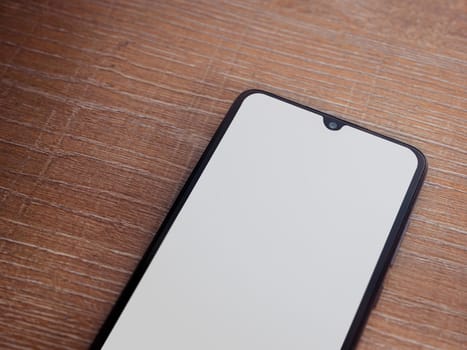 Black mobile smartphone mockup lies on the surface with blank screen isolated on wooden background. Top view closeup with selective focus and copy space, cut in the middle.