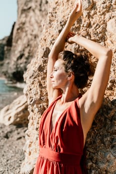 Woman red dress sea. Woman in a long red dress posing on a beach with rocks on sunny day. Girl on the nature on blue sky background