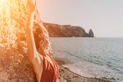 Woman red dress sea. Woman in a long red dress posing on a beach with rocks on sunny day. Girl on the nature on blue sky background