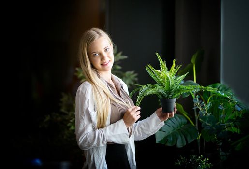 Caucasian young woman holding plants with green leaves at home. Home gardening.