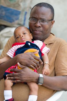 a man in glasses sitting outside holds his baby in his hands.