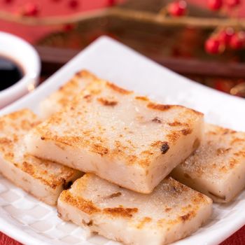 Chinese lunar new year food concept, Delicious turnip radish cake, local cuisine in restaurant with soy sauce on red background, close up, copy space