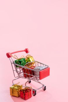 Annual sale, Christmas shopping season concept - mini red shop cart trolley full of gift box isolated on pale pink background, copy space, close up