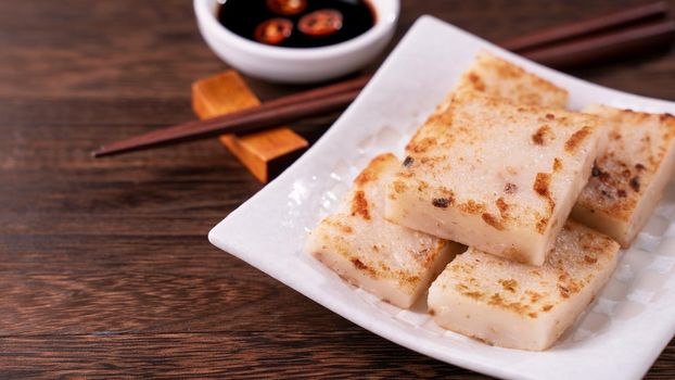 Delicious turnip cake, Chinese traditional local dish radish cake in restaurant with soy sauce and chopsticks, close up, copy space.