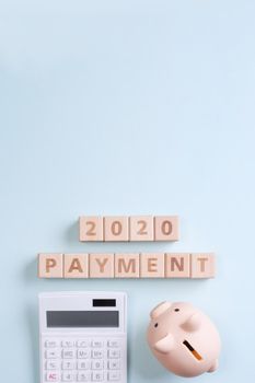 2020 goal, finance plan abstract design concept, wood blocks on blue table background with piggy bank and calculator, top view, flat lay, copy space.